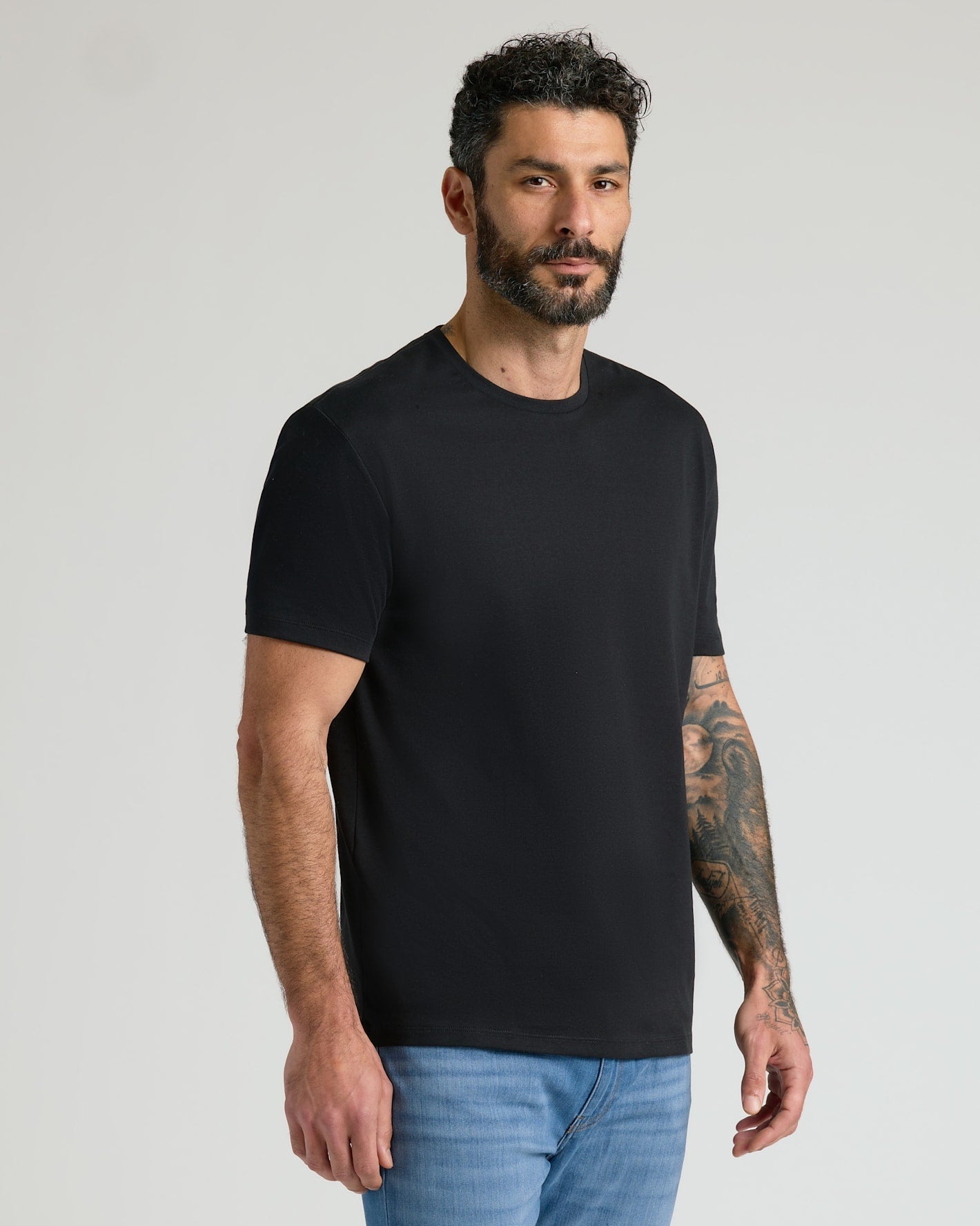 Man wearing a black Pima Cotton Blend Crew 4-Pack t-shirt paired with blue jeans, showcasing a comfortable and classic men's basics style.