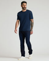 Man wearing a navy crew neck t-shirt from the Pima Cotton Blend Crew 4-Pack, paired with dark jeans and white sneakers, standing against a light background in a casual pose